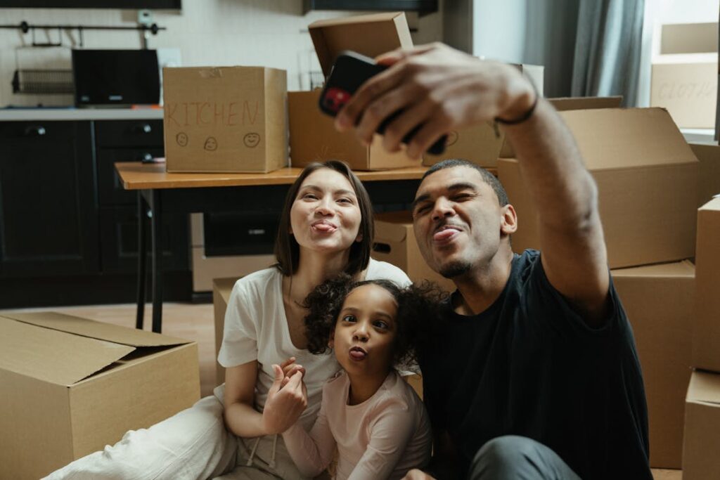 Free Happy family capturing a selfie surrounded by moving boxes, embracing their new home adventure. Stock Photo