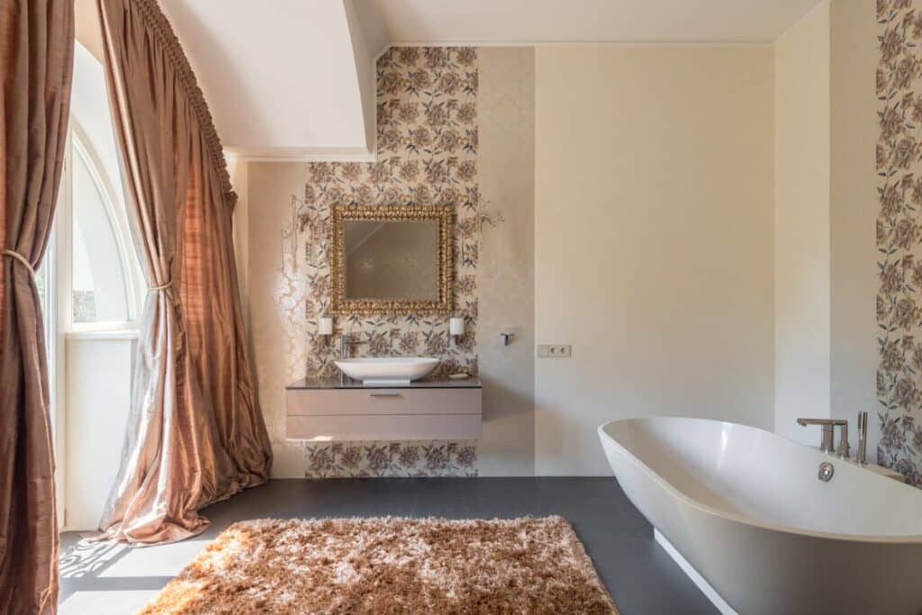 Free Spacious luxury bathroom with floral wallpaper, freestanding bathtub, and large window with curtains. Stock Photo