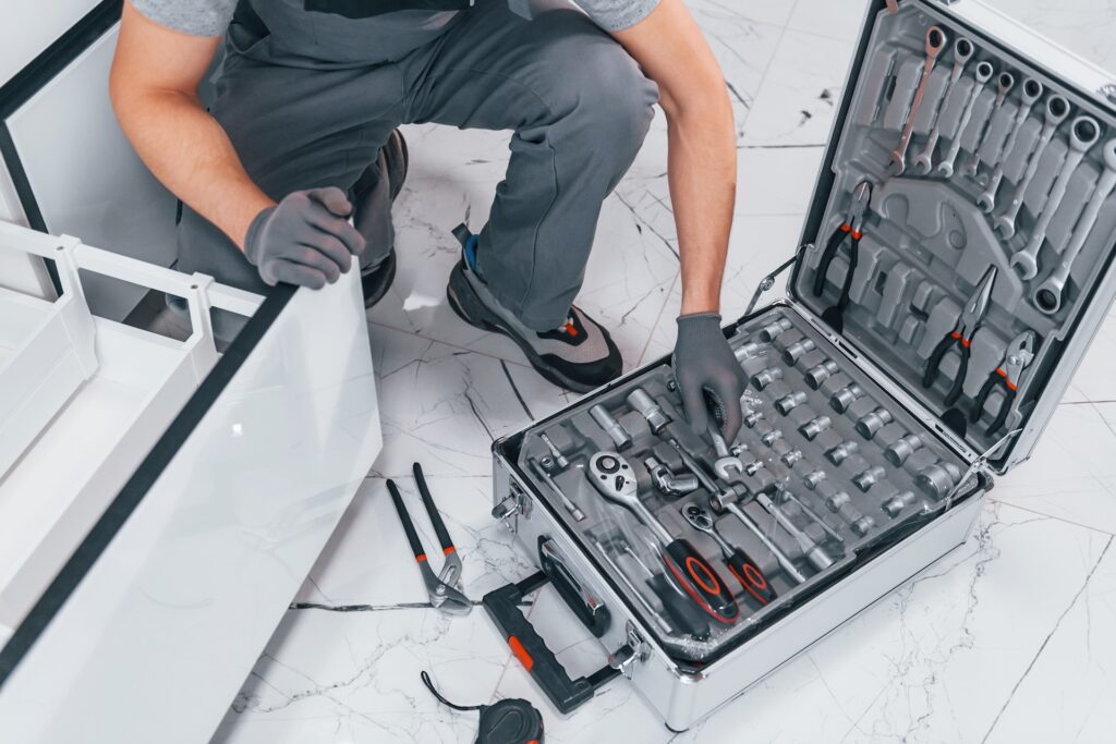Young professional plumber in grey uniform using equipment on the kitchen and preparing for the work