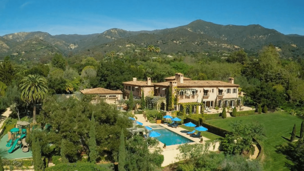 Aerial view of Prince Harry's Montecito Home with a pool and playground nestled among lush green trees and rolling mountains