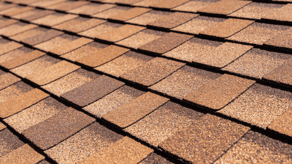 Close-up view of overlapping asphalt roof shingles in variegated shades of brown and tan.