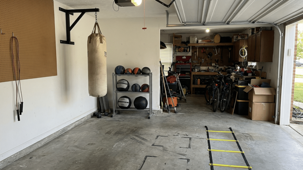 Half garage gym corner with mounted heavy bag, medicine balls, and open space for conditioning drills