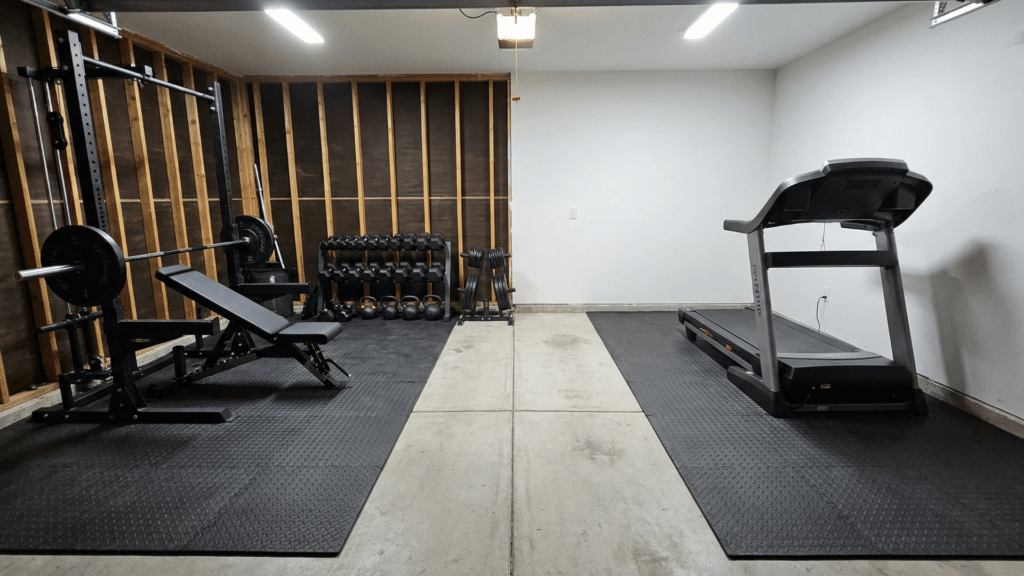 Half garage gym divided into strength and cardio zones with rack on one side and treadmill on the other