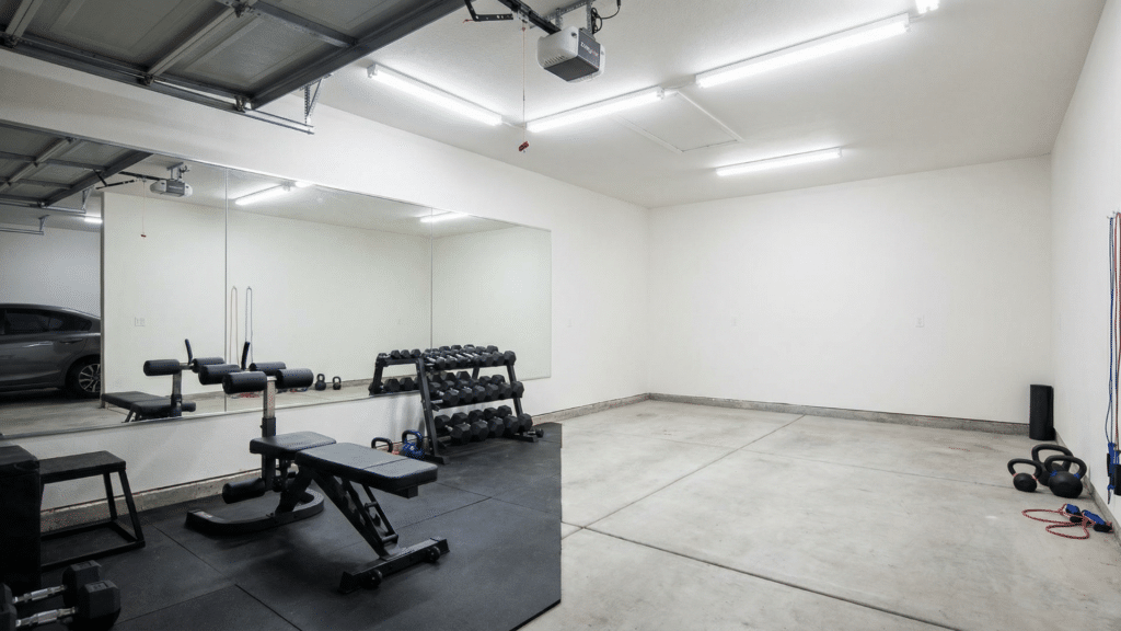 Half garage gym with large wall mirror reflecting rack and bench to create a spacious workout feel