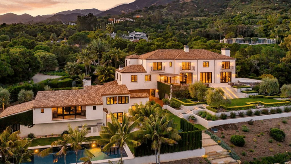 Prince Harry's estate with white stucco walls and a terracotta roof situated on a lush, forested hillside at twilight
