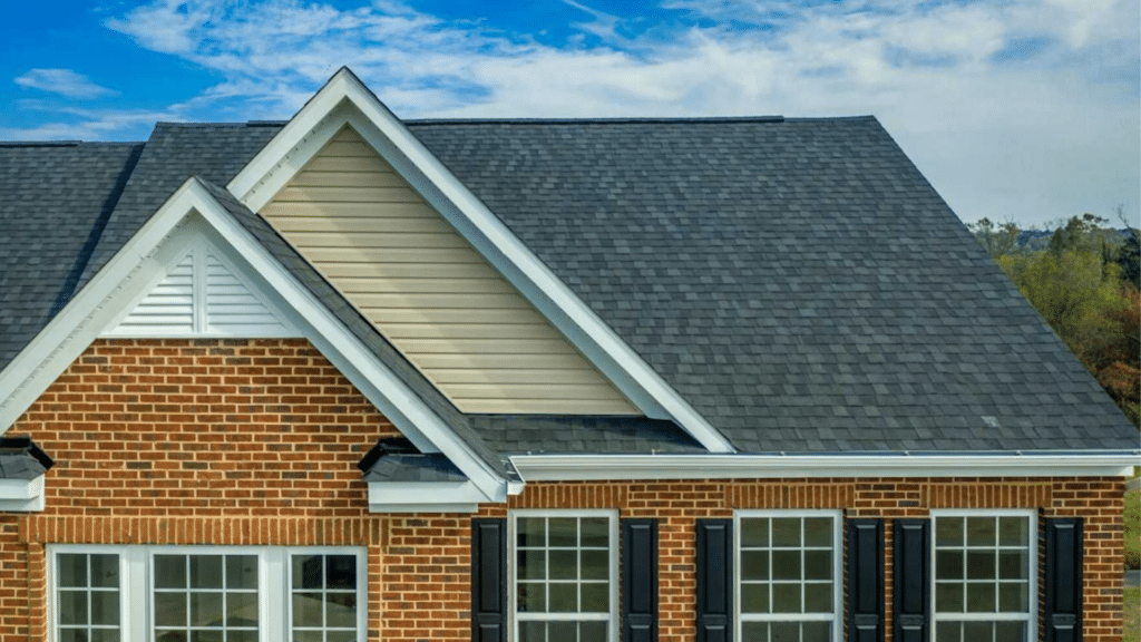 a gable roof covered with dark gray shingles which contrasts nicely with the brick facade of the house