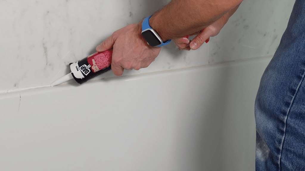 applying caulk along bathtub edge with caulking gun