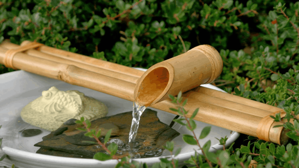 bamboo water ladle pouring water into stone bowl surrounded by greenery inspired by japanese bathroom design and garden spa style