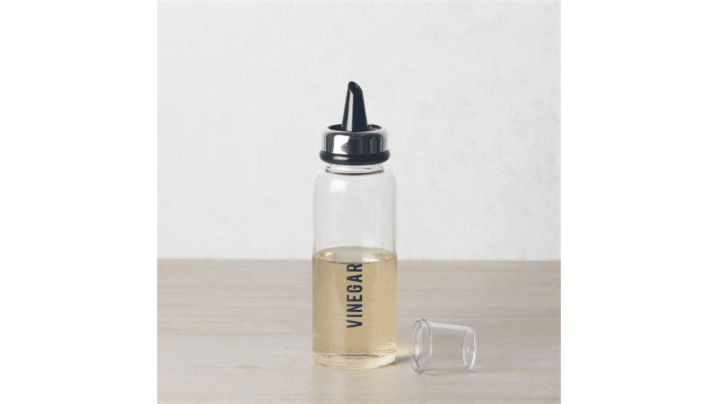 clear glass bottle labeled vinegar with metal pour spout standing on wooden table with small plastic cap placed beside it natural pest repellent