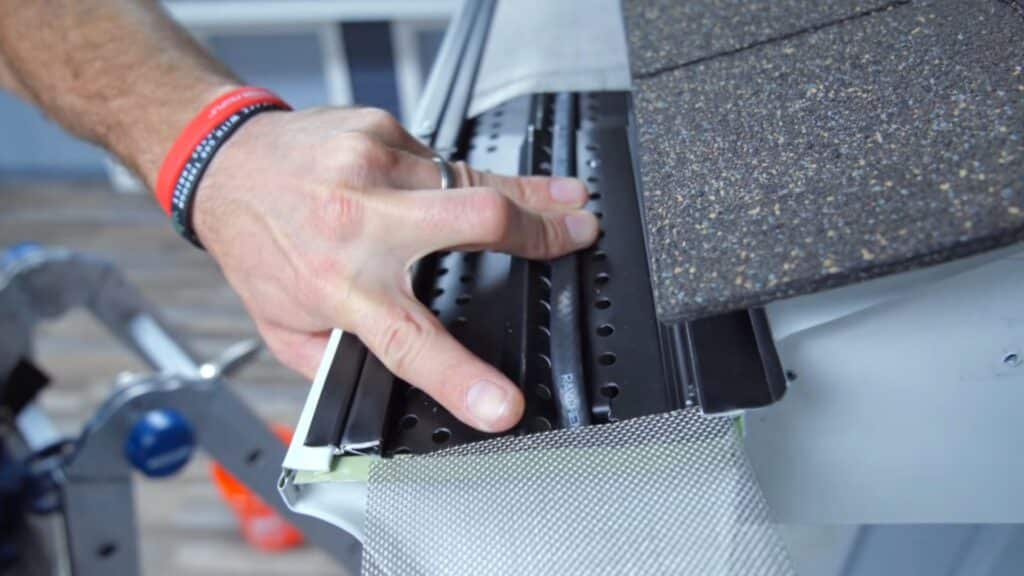 close view of hand pressing gutter guard or metal strip into place along roof edge beside textured shingles