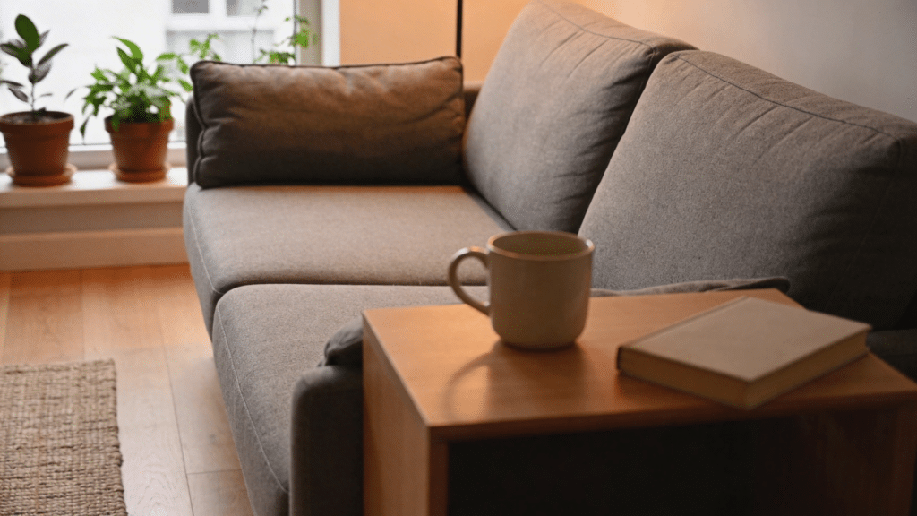 compact apartment sofa with soft fabric cushions placed beside wooden table with mug and book