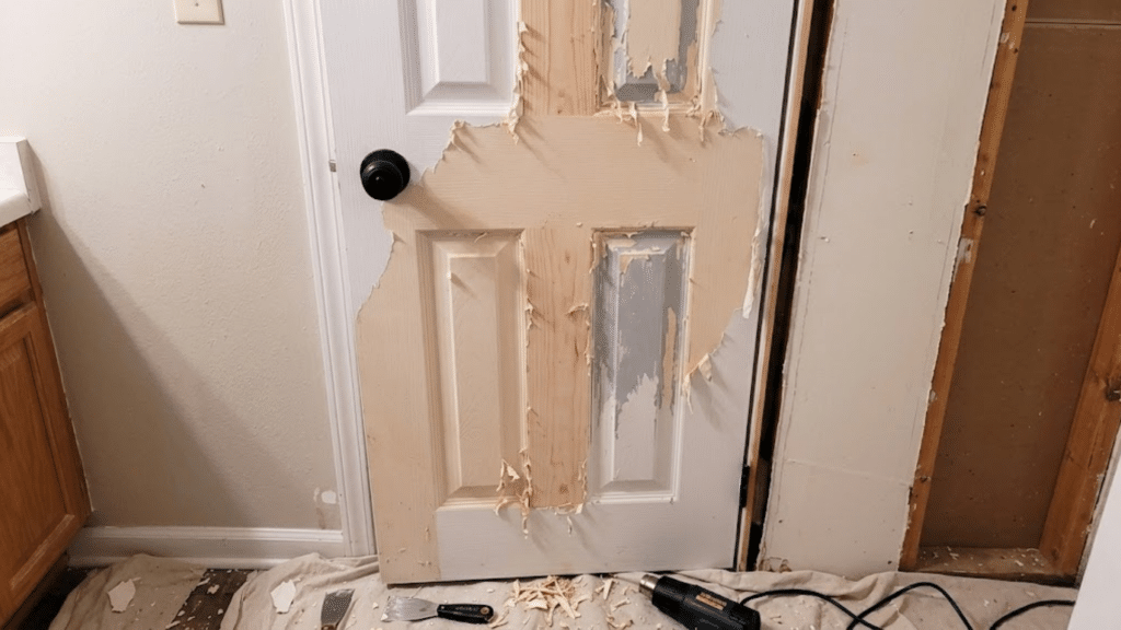 door with heavy peeling paint stripped to bare wood surface during renovation with tools