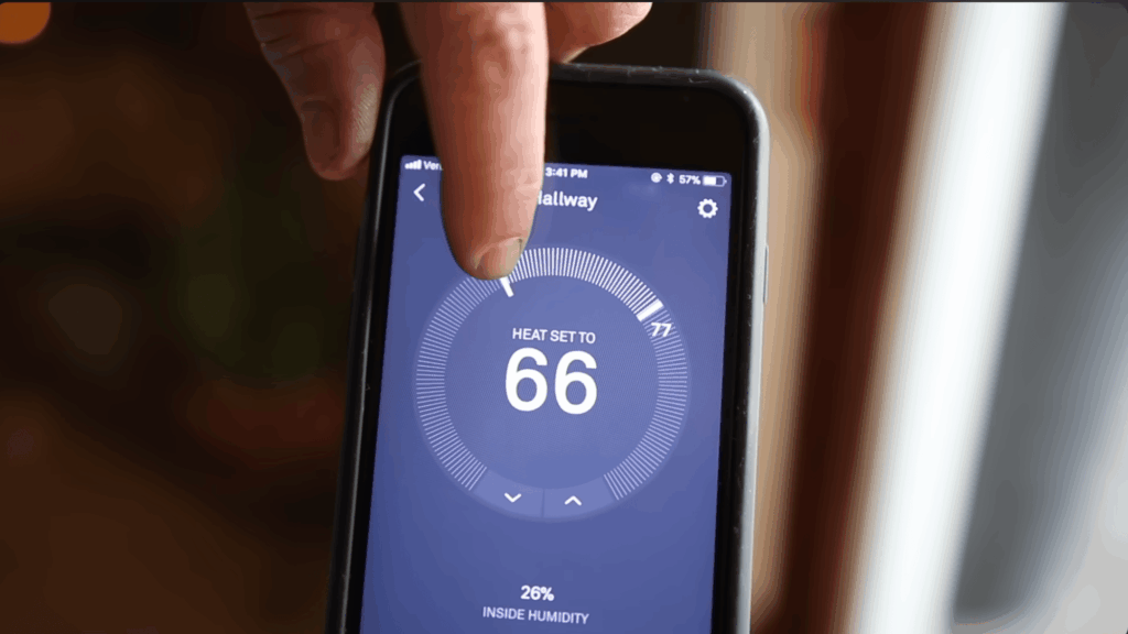 hand adjusting thermostat on phone screen showing temperature set to sixty six degrees