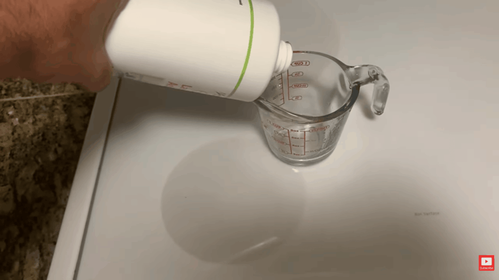 hand pouring laundry additive into measuring cup on counter demonstrating solution preparation for how to remove mold from fabric cleaning process