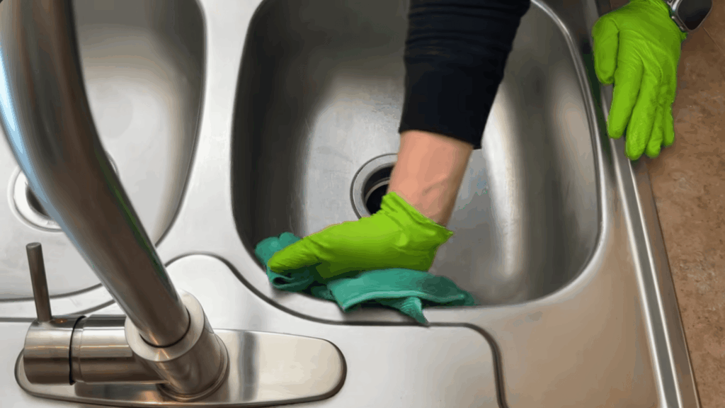hand wiping stainless steel sink with cloth final step cleaning shiny kitchen sink