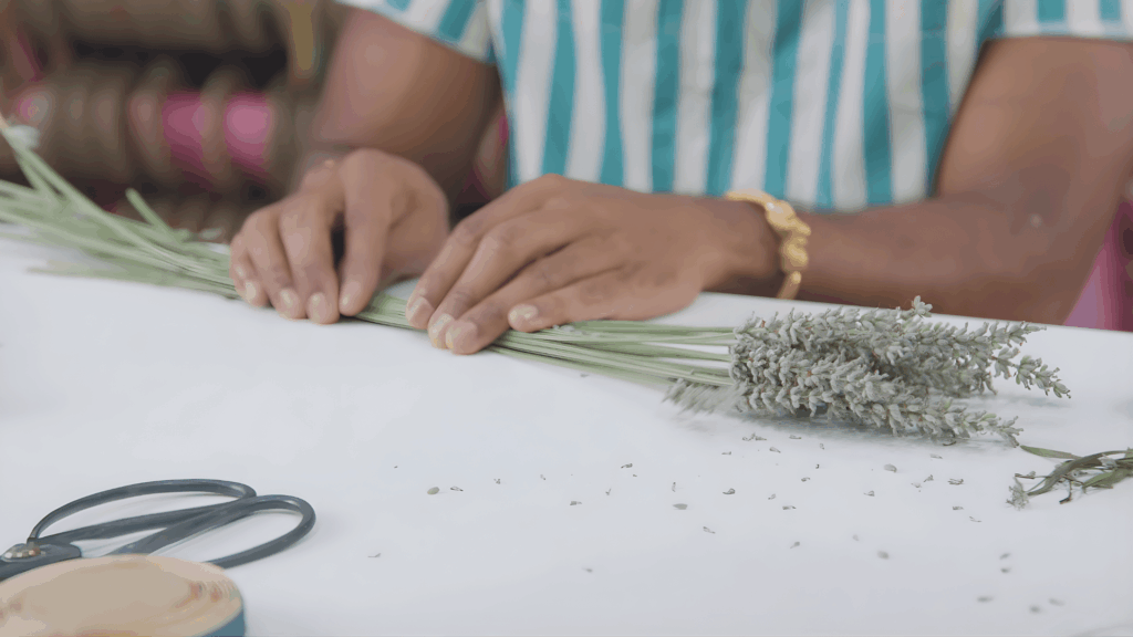 hands aligning lavender stems on table with scissors ribbon nearby