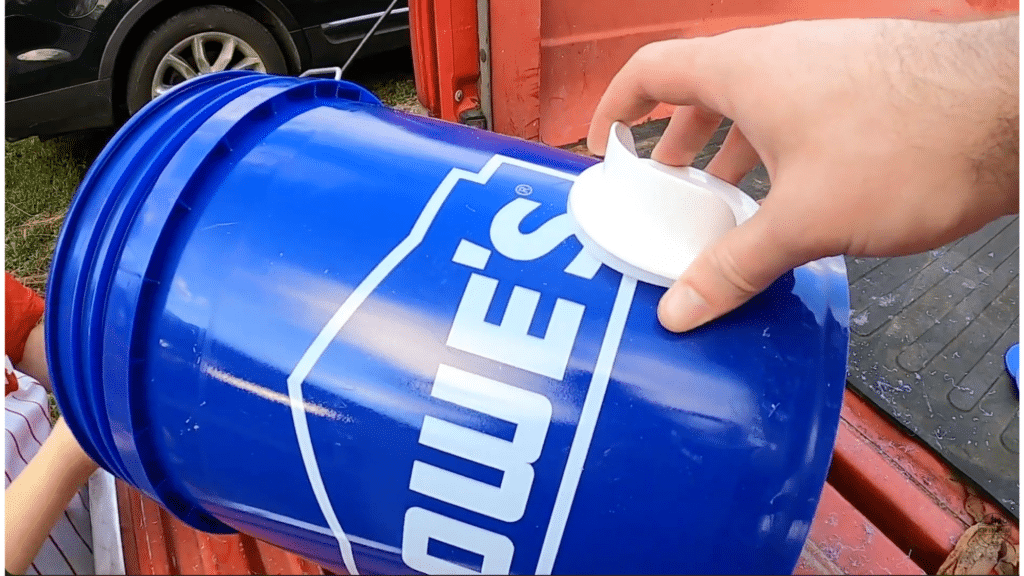 inserting feeder port into drilled bucket hole to assemble a diy chicken feeder setup