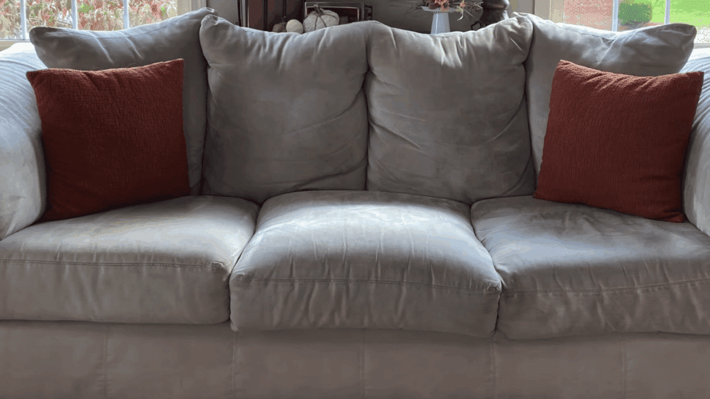 light gray sofa with three seat cushions and two orange pillows placed near window in liv