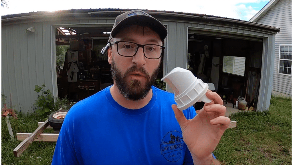 man holding a chicken feeder port attachment in front of a shed demonstrating diy feeder setup outdoors