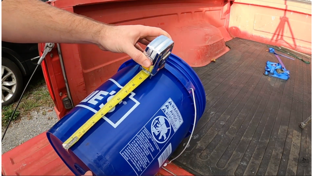 measuring 3 inches from the bottom of a blue bucket to mark drilling spots for diy chicken feeder setup