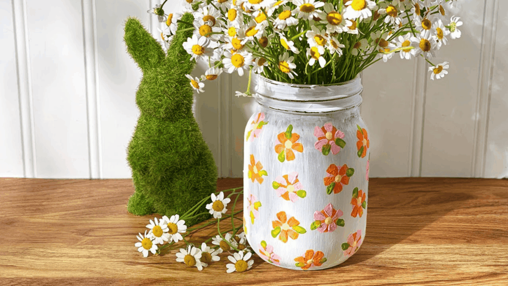 painted mason jar with small flowers holding fresh daisies beside green bunny decoration for homemade gifts made easy