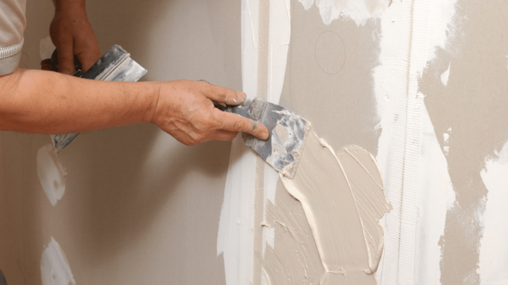 person applying joint compound on wall seam with putty knife showing plaster vs drywall finishing process