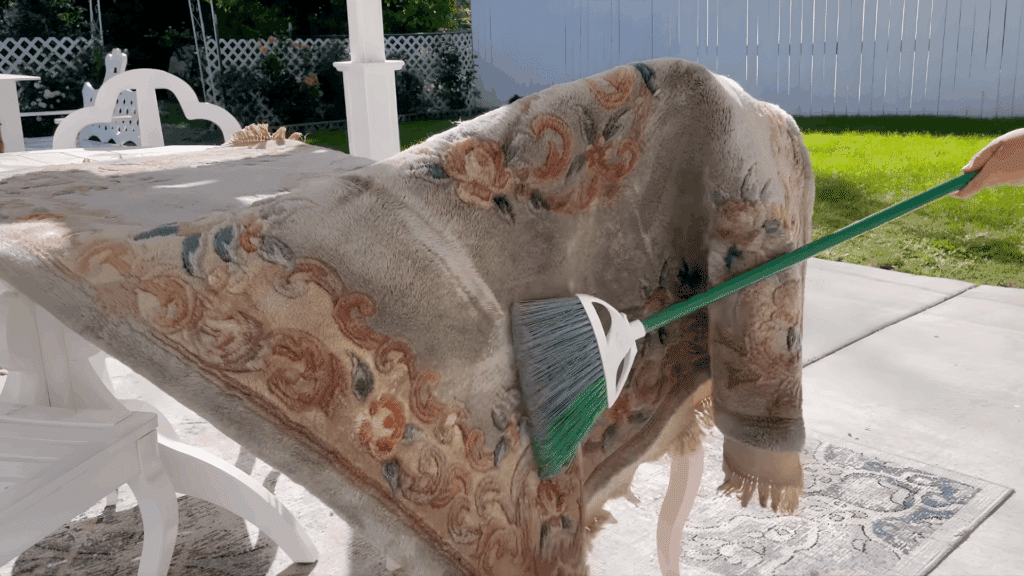 person brushing dust from a patterned wool rug outdoors on patio showing how to clean a wool rug safely and gently