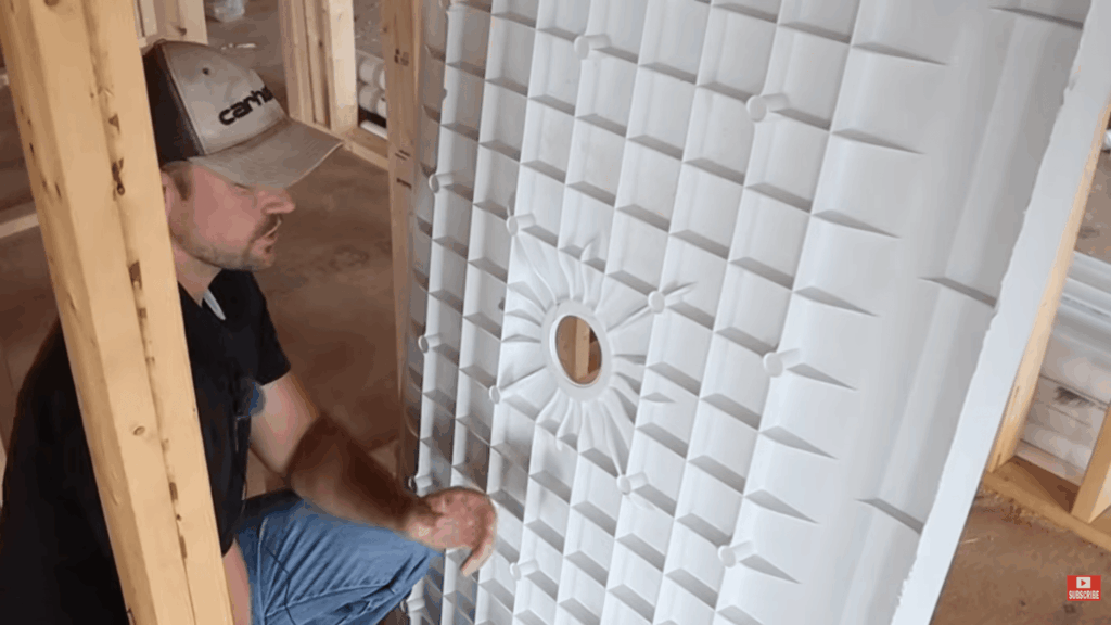person placing shower base in framed space showing how to plumb a bathroom