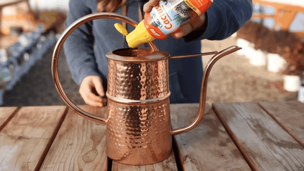 person pouring liquid plant food into copper watering can on wooden table outdoors