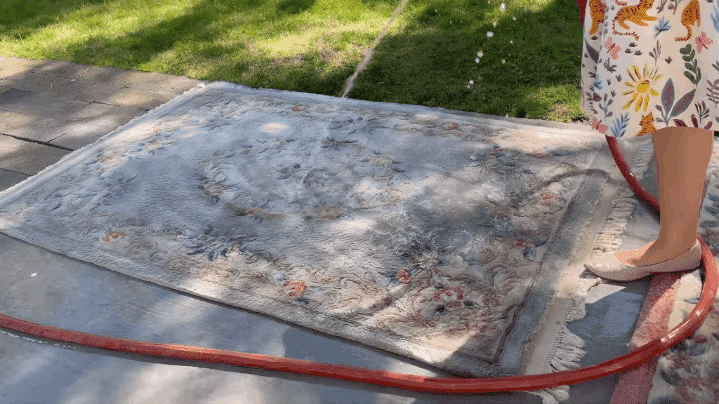 person rinsing a wool rug with water hose outdoors demonstrating how to clean a wool rug by thoroughly washing and removing soap residue