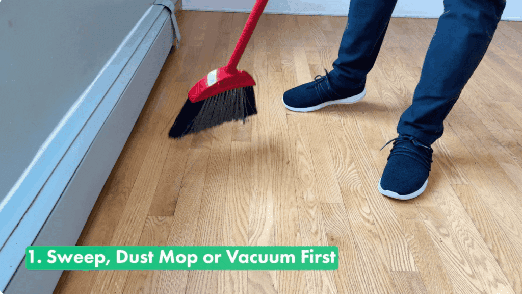 person sweeping hardwood floors with a red broom as the first step in cleaning wood floors properly