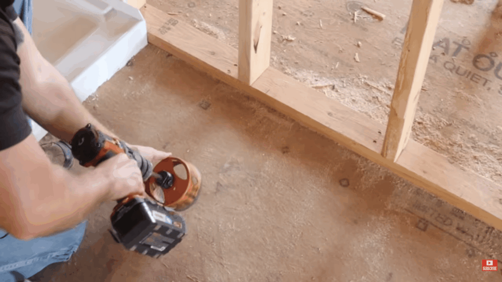 person using power tool to cut floor for pipes demonstrating how to plumb a bathroom during construction