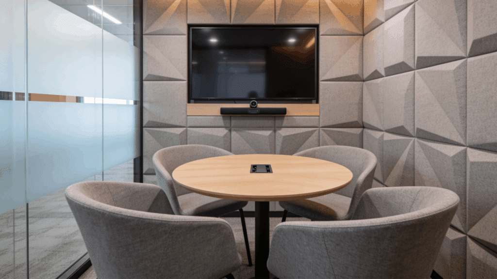 small meeting room with round table cushioned chairs wall mounted screen and acoustic panels in a modern office space