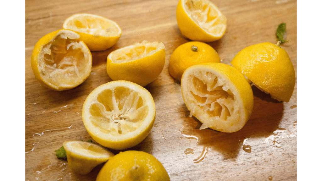 squeezed lemon halves and lemon peels scattered on wooden cutting board with visible juice and pulp after juicing fresh lemons natural pest repellent
