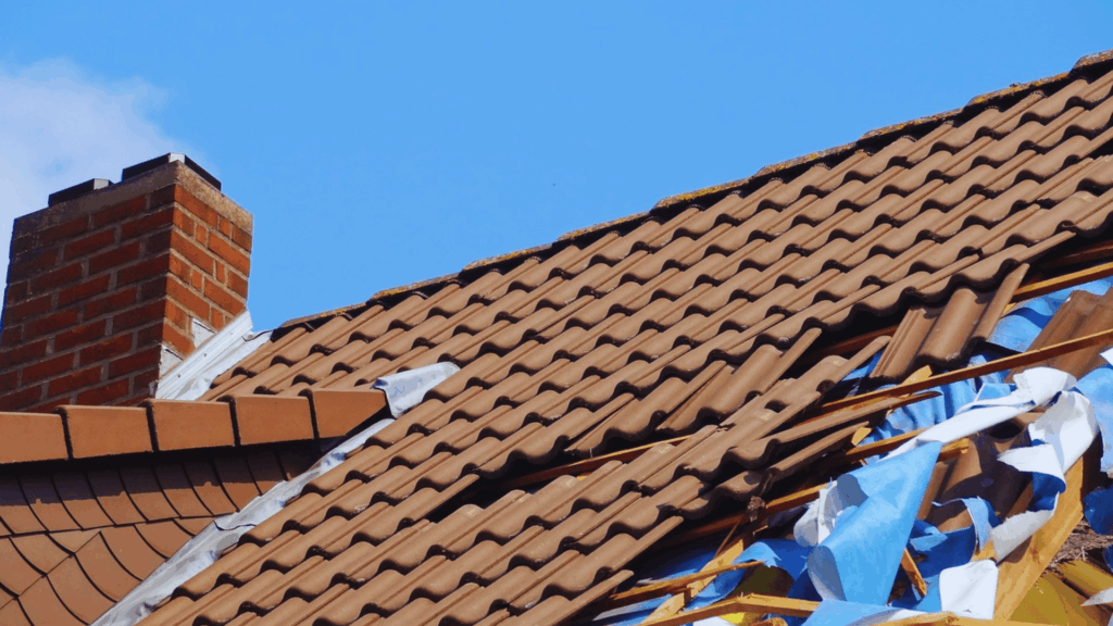 storm damaged roof with broken tiles exposed wood and debris near chimney
