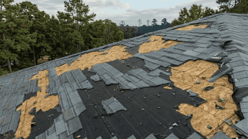 storm damaged roof with missing shingles exposed wood and torn underlayment