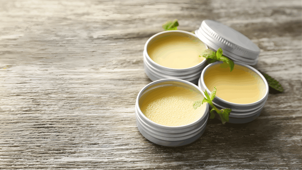 three small tins of homemade lip balm with mint leaves on wooden table for homemade gifts made easy