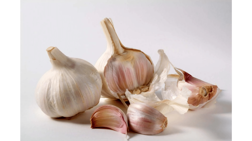 two whole garlic bulbs with several loose garlic cloves and papery skins arranged on white surface under soft natural light natural pest repellent