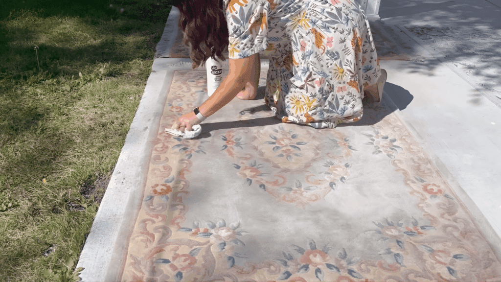 woman gently scrubbing stained wool rug with cloth outdoors demonstrating how to clean a wool rug using spot cleaning technique