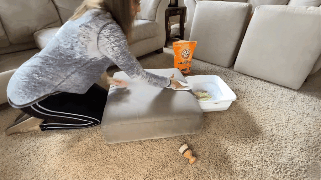 woman kneeling and wiping cushion with cloth during cleaning process in living room
