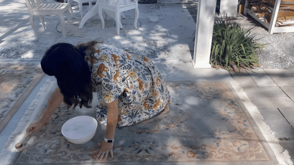 woman scrubbing wool rug with soft brush and water outdoors demonstrating how to clean a wool rug with gentle hand washing method
