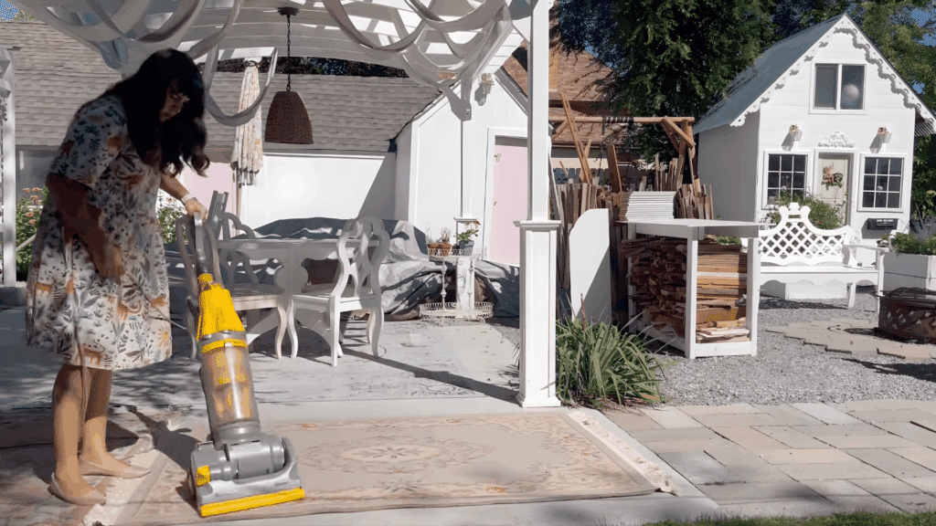 woman vacuuming a patterned wool rug on outdoor patio demonstrating how to clean a wool rug with gentle suction cleaning