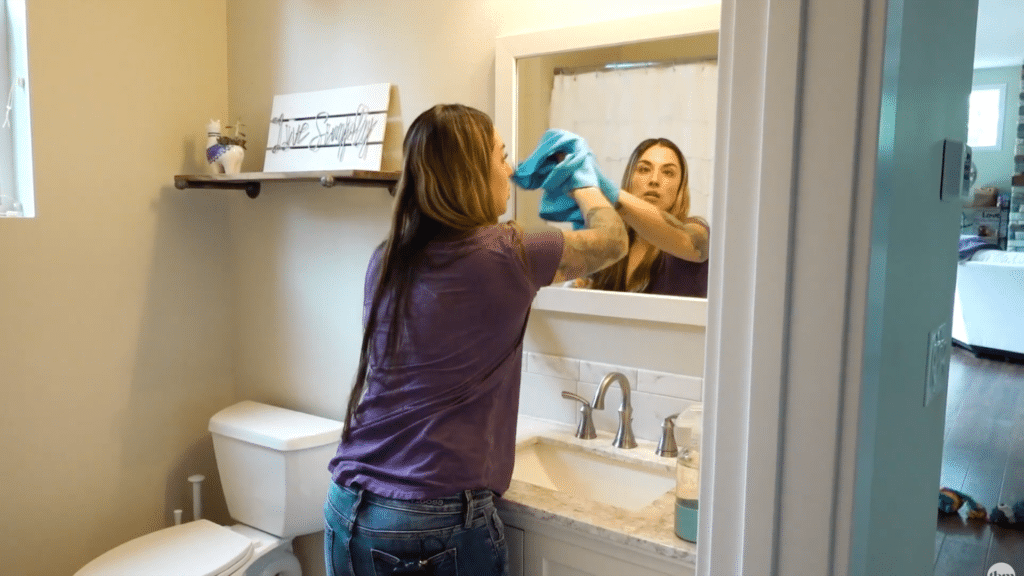woman wiping bathroom mirror with cleaning cloth
