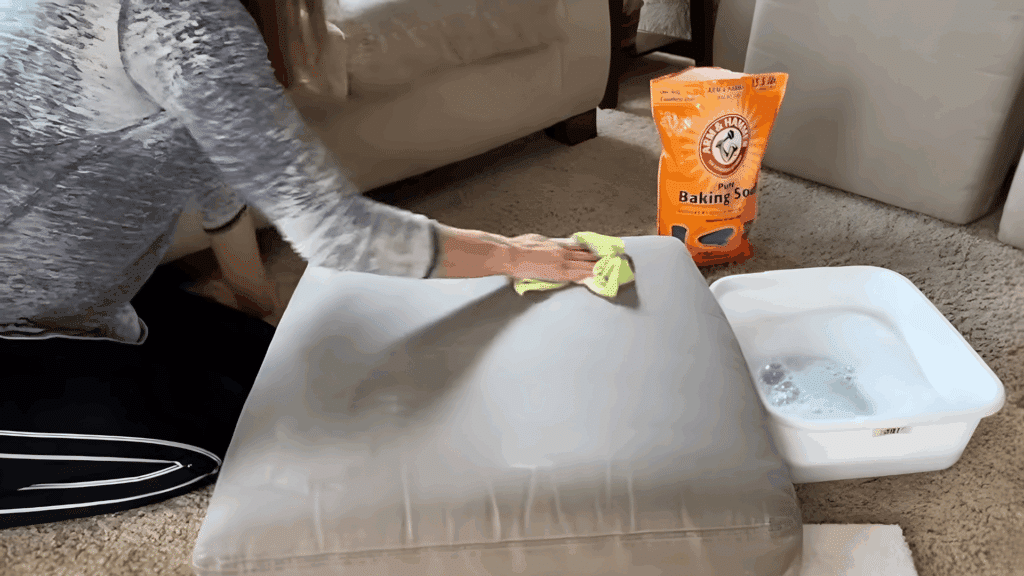 woman wiping cushion with green cloth next to bowl of soapy water on floor