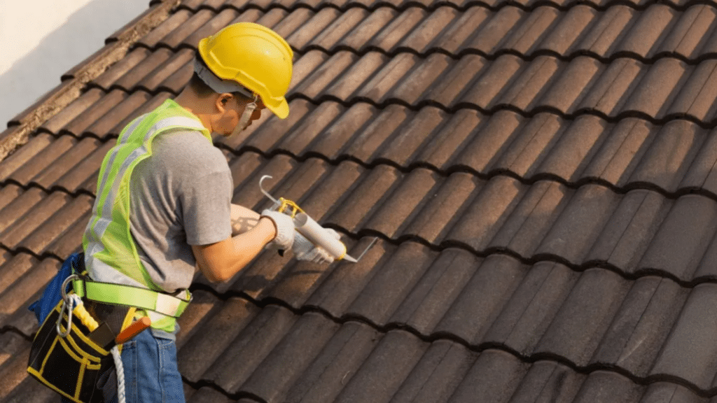 worker in safety gear applying solution during tile roof cleaning on a brown tile roof while standing carefully