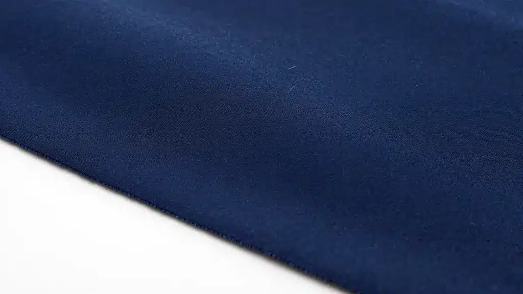 Close-up of a smooth navy blue nylon fabric, showcasing its sleek and glossy texture with visible stitching along the edges.