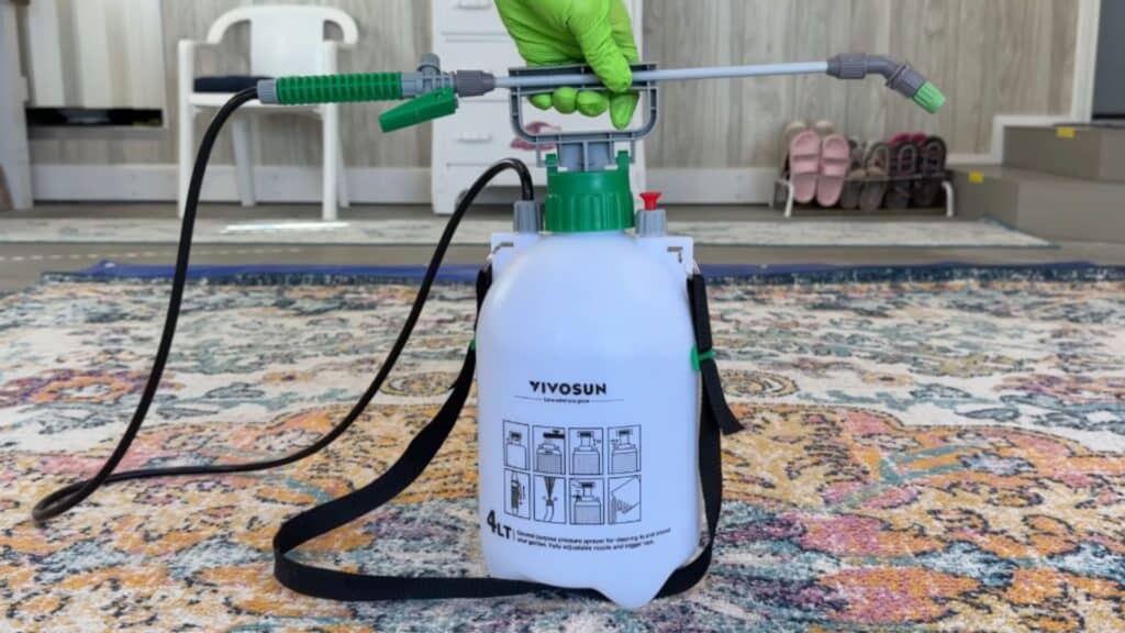 a close view of a hand holding a pressure sprayer tank used for applying cleaning solution on a rug surface