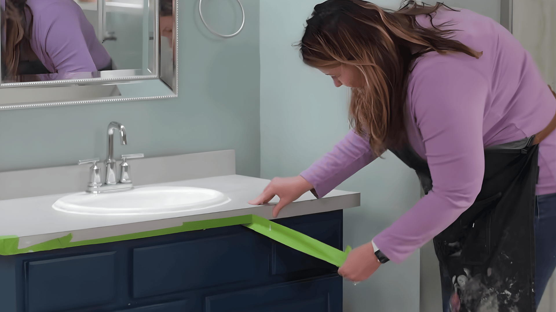 a person peels green tape from the edge of a painted cabinet beneath a bathroom sink revealing clean lines