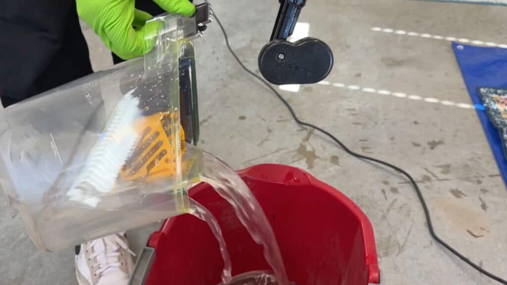 a person pouring dirty water from a carpet cleaner tank into a red bucket after washing a rug
