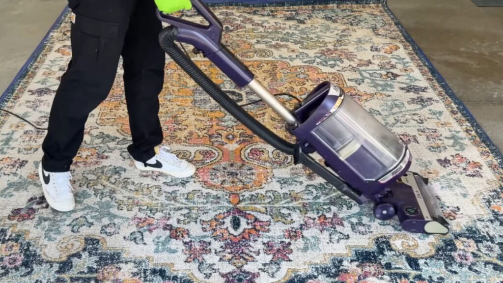 a person using a vacuum cleaner over a large decorative rug to remove dust and debris before washing